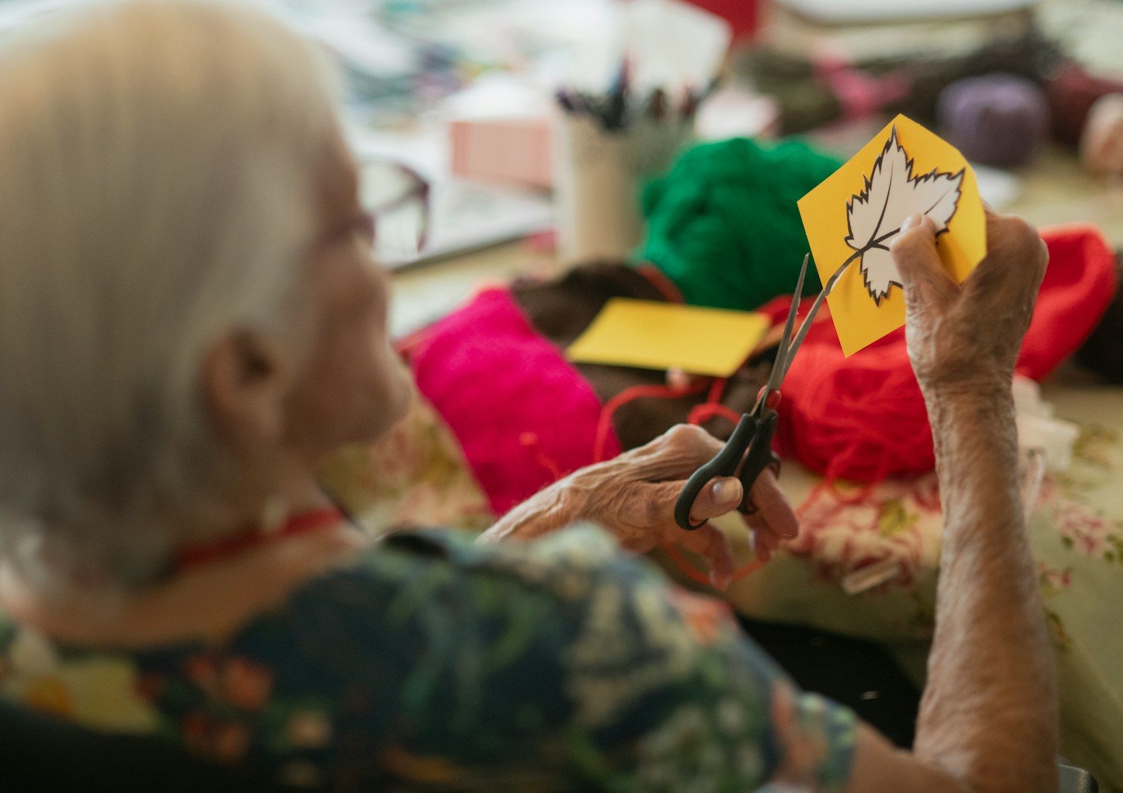 Elderly woman crafts autumn leaf decoration with scissors.
